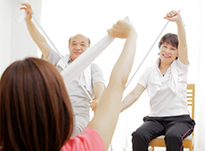 タオルを持って椅子に座ってできる運動の指導を受ける人々