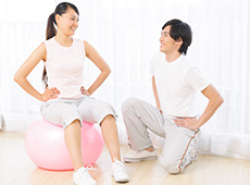 バランスボールでトレーニングする女性とそれを指導する男性トレーナー